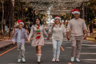 A joyful family walks down a decorated street wearing Christmas hats, symbolizing holiday spirit.